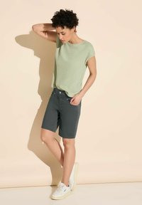 Top corto a maniche corte di un verde chiaro texturizzato abbinato a pantaloni tailored grigi scuri. Sneakers bianche completano l'outfit. Design minimalista, vestibilità casual.