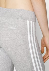 Grå träningsleggings med mjuk textur, hög midja och tre vertikala vita ränder längs sidan.