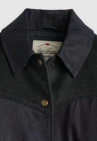 Mørk denimjakke med ullkrage, gullknapper og kontrasterende blå sømmer. Levi Strauss-merket synlig inne i kragen.
