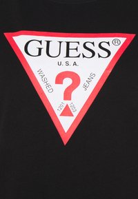 Camiseta negra con un gran gráfico en forma de triángulo rojo y blanco que incluye "GUESS U.S.A." y un signo de interrogación central, junto con las palabras "WASHED" y "JEANS."