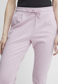 Ljust rosa joggingbyxor i mjukt tyg, med ett elastiskt midjeband med knytning, och två sidofickor för bekvämlighet.