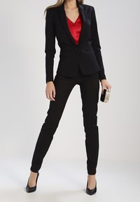 Svart skräddarsydd blazer över en röd blus, tillsammans med svarta figurnära byxor och svarta högklackade skor. Accessoarer inkluderar en liten, dekorerad clutch.