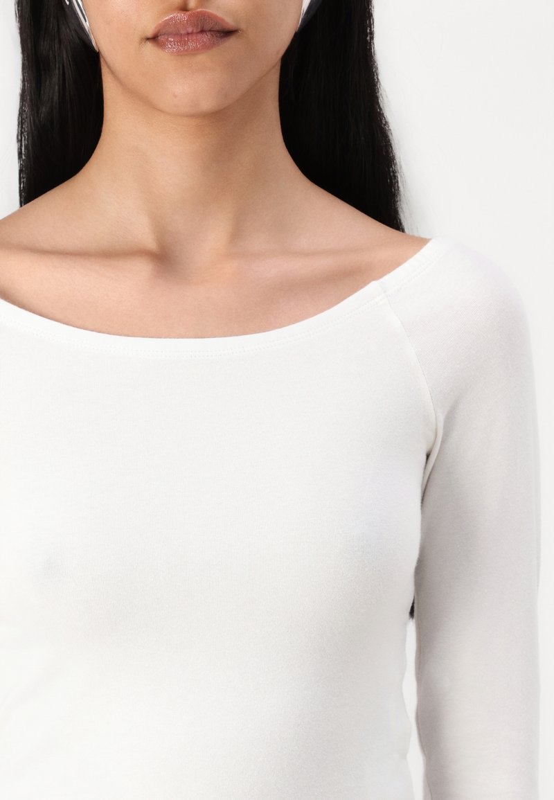 Maglietta bianca a maniche lunghe realizzata in un tessuto morbido con scollatura rotonda, caratterizzata da una texture liscia e un design aderente.