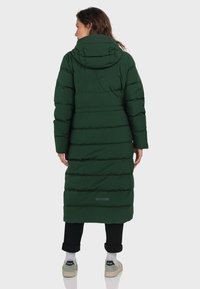 Langer, grüner Puffermantel mit horizontalen Steppabschnitten, Kapuze und elastischen Bündchen; verfügt über ein Logotag nahe dem Saum und wird mit lässigen Schuhen kombiniert.