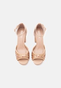 Beige hakken sandaaltjes met glinsterende gouden versieringen op de voorste band, een verstelbare enkelband en een blokhakontwerp.