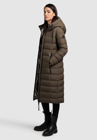 Langer, olivgrüner Daunenmantel mit Kapuze, Frontreißverschluss und Taschen. Verfügt über ein gestepptes Muster und ein glattes Innenfutter.