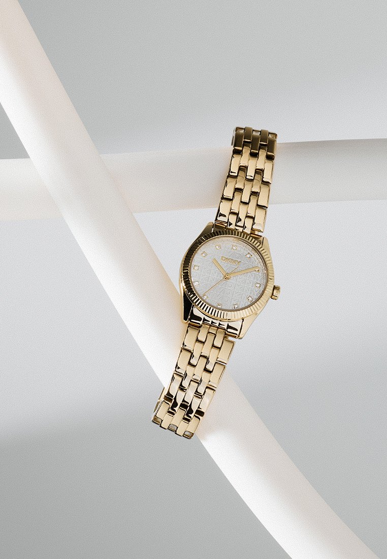 Reloj de metal en tono dorado con una esfera blanca texturizada, marcadores de hora dorados y un diseño de brazalete enlazado. Presenta un bisel acanalado.