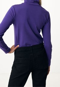 En figurnära lila långärmad top i kombination med högmidjade svarta jeans. Toppen har en ståkrage, medan jeansen har bakfickor.