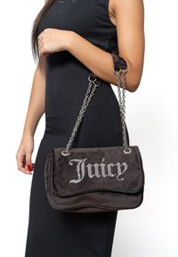 Graue Wildleder-Handtasche mit Klappenverschluss, silberner Kettenriemen und Strass-Buchstaben, die "Juicy" buchstabieren. Glatte Textur und runde Form.
