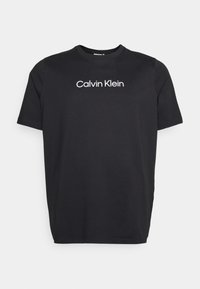Schwarzes Baumwoll-T-Shirt mit kurzen Ärmeln und Rundhalsausschnitt, das ein weißes „Calvin Klein“-Logo auf der Brust in der Mitte trägt.