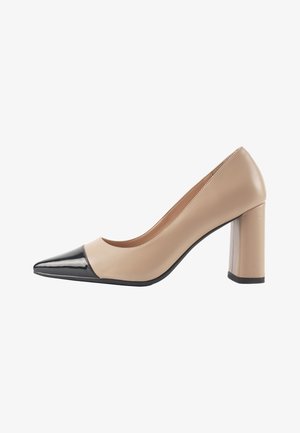 Zapatos de tacón alto de piel beige con punta afilada, que presentan una puntera en charol negro y un tacón cuadrado grueso. Textura suave, diseño minimalista.