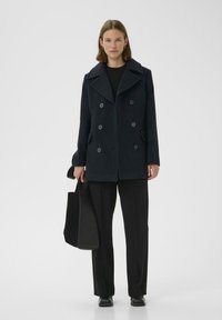 Jūrinė dvigubo užsegimo striukė su didelėmis apykaklėmis, juodais mygtukais ir šoninėmis kišenėmis. Derinama su juodomis kelnėmis ir laikoma juoda rankine.