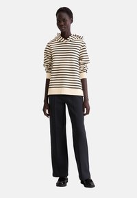 Gestreepte hoodie in beige en donkerbruin met een trekkoordcapuchon, gecombineerd met zwarte brede broek en zwarte schoenen.