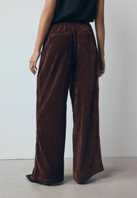 Weit geschnittene, burgunderfarbene Samthose mit strukturiertem Finish, ausgestattet mit einem hohen Bund und zwei Gesäßtaschen.