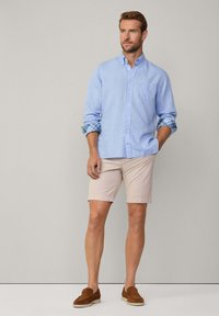 Vaaleansininen pitkähihainen nappipaita, ruudulliset hihansuut. Yhdistetty vaaleanbeigeihin shortseihin ja ruskeisiin loafer-kenkiin. Paidassa on rintatasku.