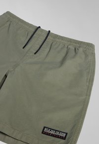 Green shorts made of lightweight fabric, featuring an elastic waistband with a drawstring and a logo patch on the lower left side.