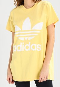 Yellow cotton t-shirt featuring a large white Adidas logo and three horizontal stripes; short sleeves and a crew neckline.