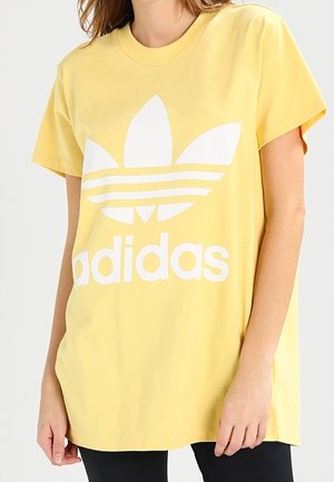 Żółta bawełniana koszulka z krótkim rękawem, z dużym białym logo Adidas oraz trzema poziomymi paskami; okrągły dekolt.