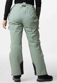 Water-resistant snow pants in light green with black accents, adjustable straps, zippered pockets, and reinforced lower legs.
