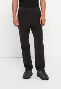 Dark brown corduroy pants with a relaxed fit, featuring a button closure and an elastic waistband, paired with textured black sneakers.