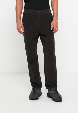 Dark brown corduroy pants with a relaxed fit, featuring a button closure and an elastic waistband, paired with textured black sneakers.