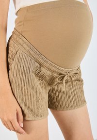 Beige těhotenské šortky s texturovaným tělem, elastickým pasem a detaily se šňůrkou. Vybaveny vroubkovaným designem pro pohodlí a flexibilitu.
