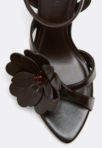 Sandale en cuir noir à bout pointu, fines brides et grande fleur décorative avec des perles près de la bride avant.