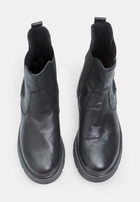 Botines de cuero negro con paneles elásticos en los laterales, punta redondeada y acabado texturizado. Presentan una asa para facilitar su uso y una suela de goma gruesa.