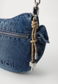 Denimowa torba na ramię o zaokrąglonym kształcie, z zamkiem błyskawicznym, teksturowanym materiałem oraz brązowym sznurkiem z metalowymi akcentami.