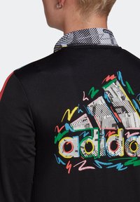 Black jacket featuring a multi-colored graphic design with "adidas" text. The collar has a patterned fabric, adding texture and visual interest.