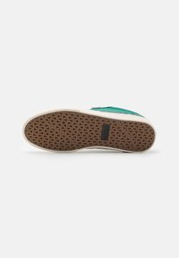 Zöld velúr sneaker, texturált barna gumitalppal és fehér középtalppal. Minimalista dizájnnal rendelkezik, és téglalap alakú márkalogó található a talpon.