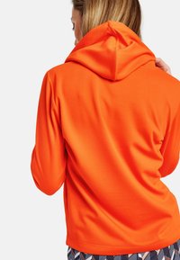 Sudadera de color naranja brillante con un acabado texturizado, mostrando una vista trasera y una capucha adjunta. Diseño simple sin hardware ni patrones visibles.