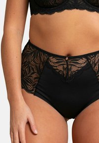 Culotte noire taille haute avec un dessus en dentelle florale et une taille lisse. Bords délicats en forme de vague et un petit bouton décoratif à l'avant.