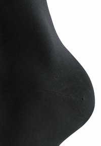Calza nera in nylon con texture liscia, design aderente e forma ergonomica curvata. Presenta una cucitura rinforzata sulla punta.