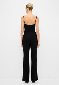 Top de tirantes finos negro con canalé, combinado con pantalones negros de cintura alta que tienen un diseño de pierna acampanada y un detalle de bolsillo en la parte trasera.