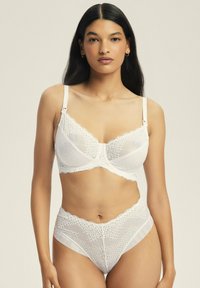 Weißer Spitzen-BH und passender hochgeschnittener Slip. Der BH hat einen gewellten Ausschnitt und verstellbare Träger. Der Slip hat eine gemusterte Textur und einen glatten Bund.