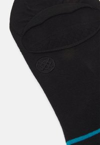 Schwarze Socke mit einem tiefen Schnitt, ausgestattet mit einem türkisfarbenen Streifen und einem runden Logo an der Seite. Hergestellt aus weichem, strukturiertem Material.