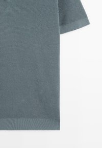 Polo à manches courtes en tissu texturé bleu clair, avec col et poignets côtelés et un ourlet coupé net.