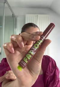 Tube d'huile à lèvres marron avec un capuchon vert et un texte audacieux en blanc et vert. Le design présente une forme cylindrique élégante avec une finition brillante.