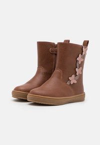 Brązowe botki za kostkę z sztucznej skóry, o teksturowanej powierzchni, z bocznym zamkiem błyskawicznym i różowymi kwiatowymi akcentami wzdłuż boku. Gumowa podeszwa zapewnia przyczepność.
