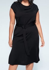 Schwarzes kurzes Kleid mit kurzen Ärmeln, rundem Ausschnitt und einem Stoffgürtel. Glatte Textur, knielang und mit Seitenschlitzen für zusätzlichen Komfort.