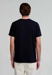 Tricou negru din bumbac, cu mâneci scurte, guler rotund și un design simplu pe spate. Materialul pare neted și flexibil, fără modele sau accente vizibile.