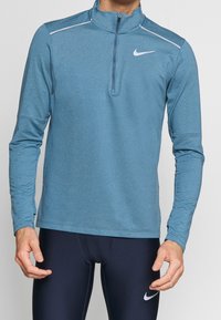 Maglia atletica blu a maniche lunghe con collo a mezza zip, accenti bianchi, tessuto elasticizzato e design aderente, adatta per sport o esercizio.