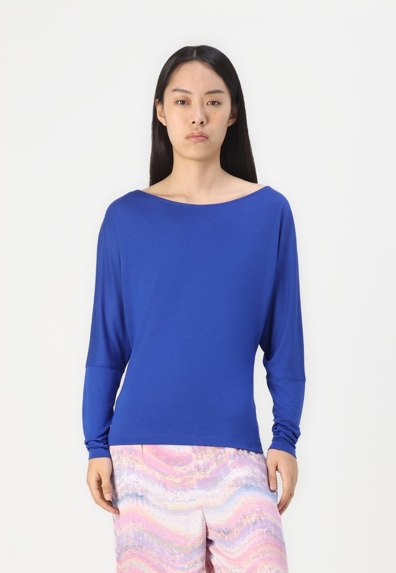 Blaues Langarmshirt mit weitem Ausschnitt und lockerer Passform, aus weichem Material. Kombiniert mit pastellfarbenen gemusterten Hosen.
