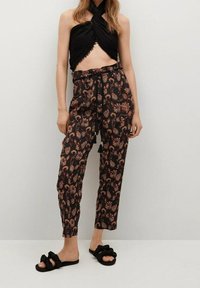 Zwarte crop top met knoopdetail, gecombineerd met zwarte broeken met bloemenpatroon in oranje en beige tinten. Zwarte instappers.