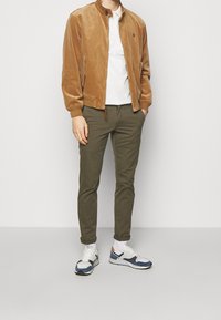 Tan corduroy bomber jacket, white polo shirt, olive green pants, and white sneakers with blue and orange accents.