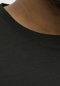 Gros plan sur un tissu de t-shirt noir montrant un col rond avec des coutures fines, une texture lisse et un léger reflet à la surface.