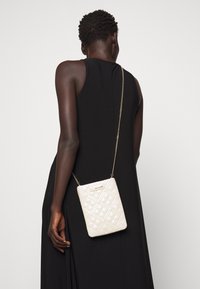 Borsa a tracolla bianca trapuntata con una catena dorata, caratterizzata da una forma rettangolare e un dettaglio del logo stampato sul davanti.