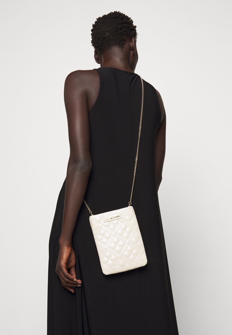 Borsa a tracolla bianca trapuntata con una catena dorata, caratterizzata da una forma rettangolare e un dettaglio del logo stampato sul davanti.