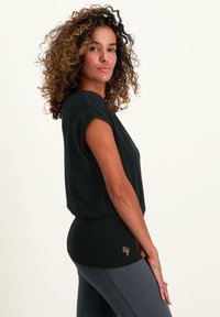 Svart kortärmad topp med en avslappnad passform och lätt kontur vid midjan. Har en liten broderad logga i orange vid fållen.